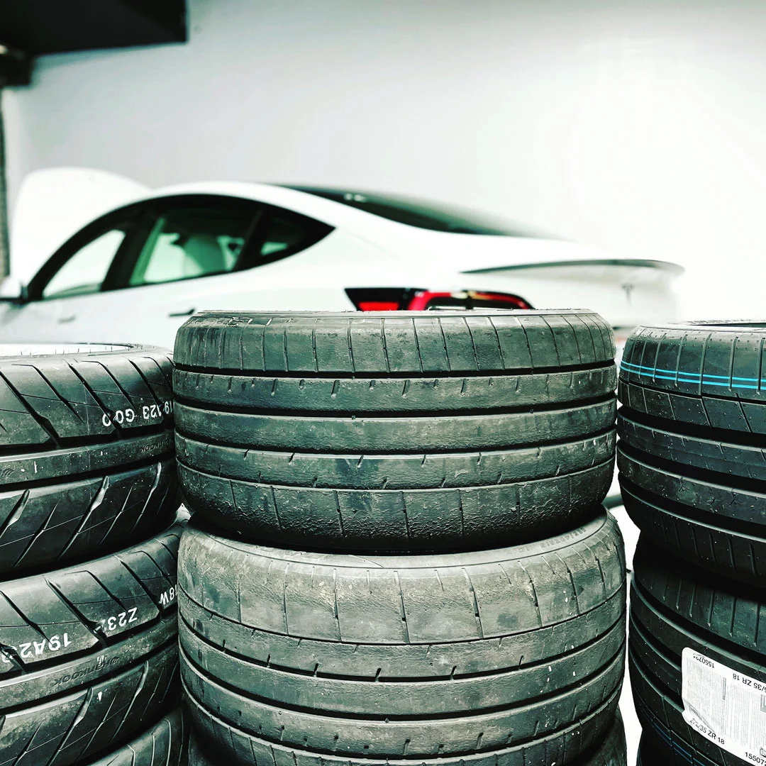 Stacks of tires behind a Tesla Model 3.